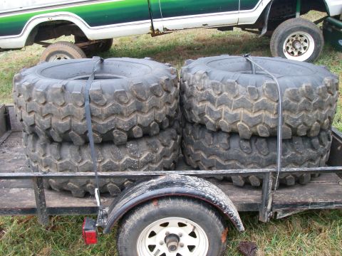 1978 Ford Bronco - A trailer carries four large off-road tires, with a portion of a green and white truck visible in the background.