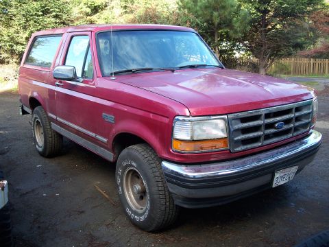 1977 Ford F-150 - This red Ford Bronco is parked outdoors on a dirt surface with trees in the background.