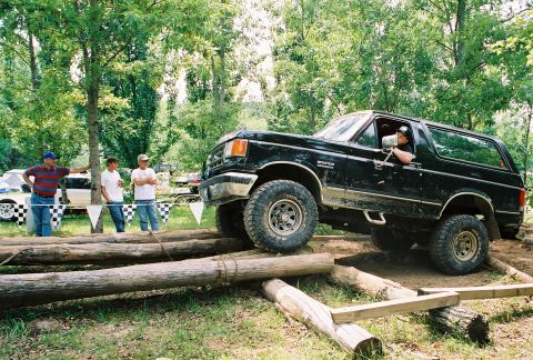 1991 Ford Bronco - A black Ford Bronco navigates a challenging log obstacle during an off-road event.