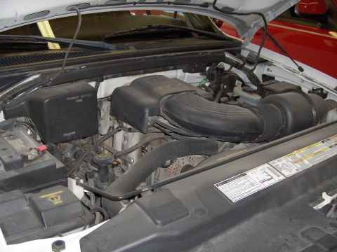2007 Ford Mustang - Engine bay of a white Ford truck or SUV viewed from the driver's side with the hood open, showing the black plastic engine cover, airbox wi…