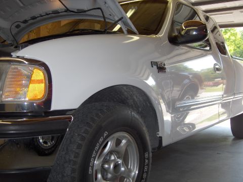 2007 Ford Mustang - Low close-up along the passenger-side front fender of a white late-1990s Ford F-150 with the hood raised, showing the amber corner lamp, ch…