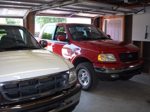 2007 Ford Mustang - Two Ford trucks, a red F-150 and a white truck, are parked inside a garage.
