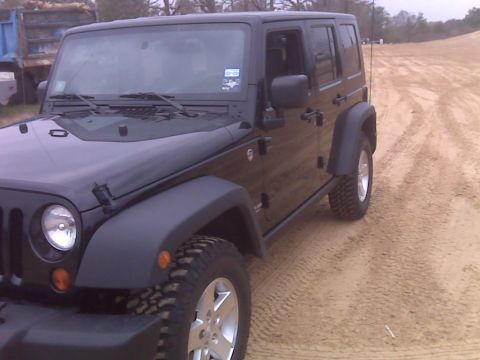 2008 Jeep Wrangler - Black 2008 Jeep Wrangler parked on a sandy surface with a dump truck in the background.