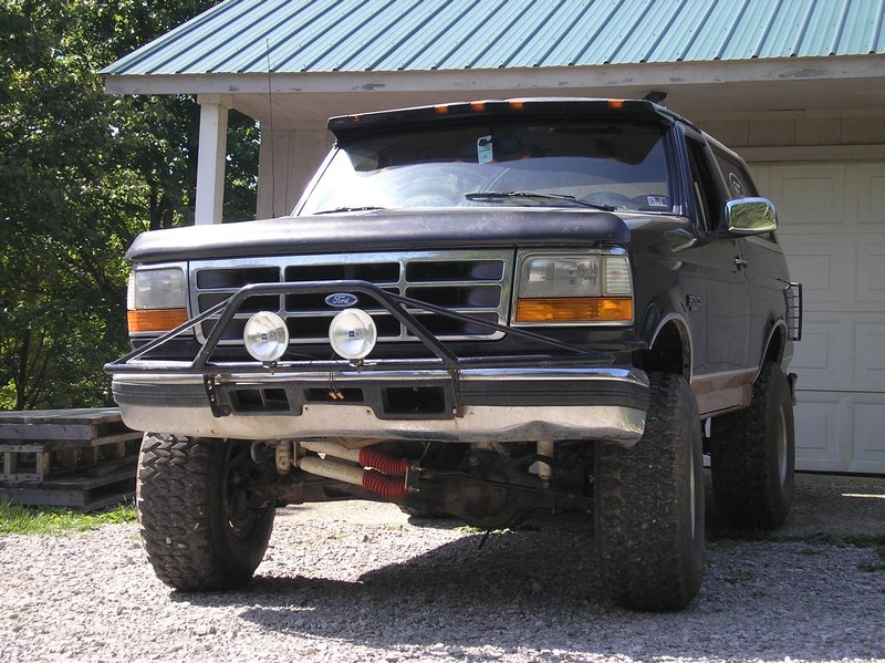 Black lifted Ford Bronco SUV with brush guard, driving lights and mud tires on gravel