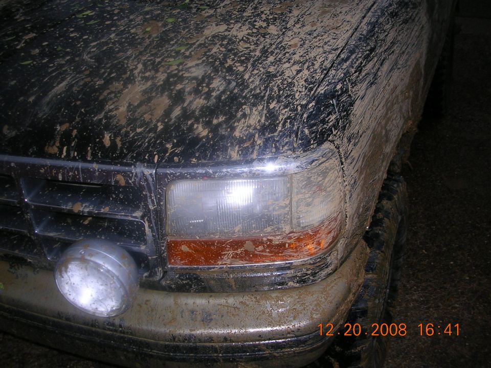 Mud-covered black SUV front corner with a round auxiliary light and orange turn signal