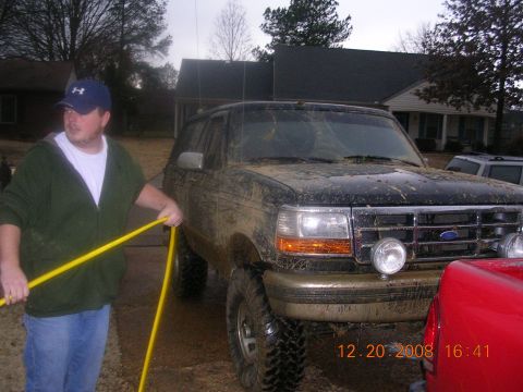 1994 Ford Bronco - Man washes a muddy 1994 Ford Bronco in a driveway on a cloudy day.