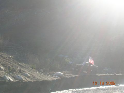 1985 Ford Bronco - A red SUV flies an American flag while parked on a dirt embankment next to a body of water.
