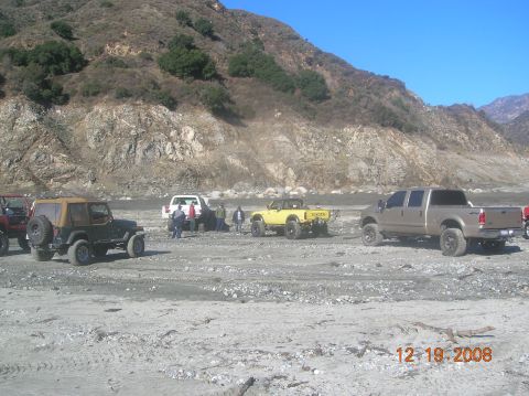 1985 Ford Bronco - Off-road vehicles gathered on a dry riverbed with a mountainous backdrop under a clear blue sky.