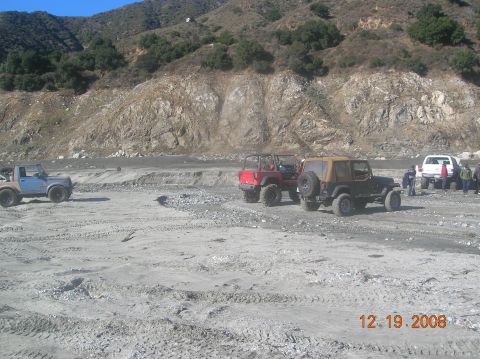 1985 Ford Bronco - Several off-road vehicles are gathered in a dusty, rocky terrain with a mountain in the background.
