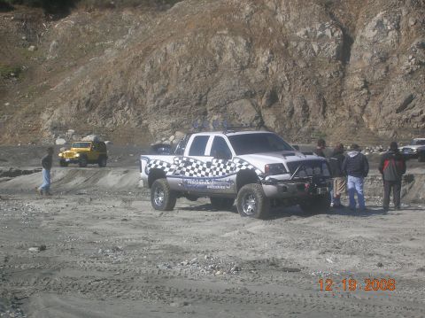 1985 Ford Bronco - A white pickup truck with checkered graphics is parked on a dirt lot with a yellow Jeep in the background.