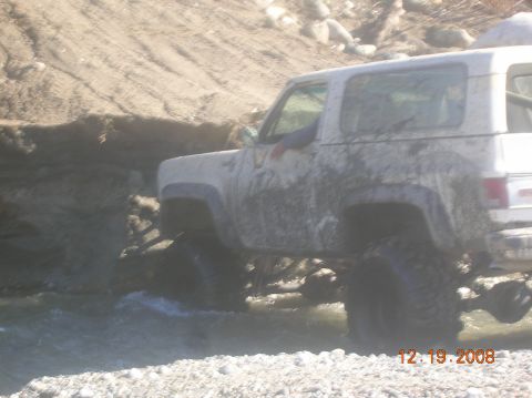 1985 Ford Bronco - A white SUV navigates a muddy, watery terrain, its tires submerged.
