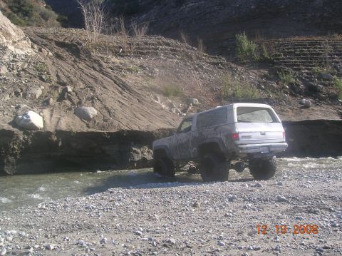 1985 Ford Bronco - A white SUV navigates a rocky stream bed, its large tires suggesting off-road capability. The date 12.19.2008 is visible in the lower right…