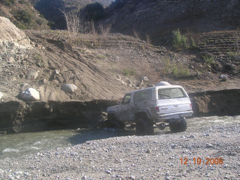 1985 Ford Bronco - GMC SUV navigates a rocky stream bed in a , natural environment.