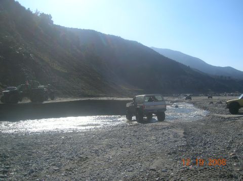 1985 Ford Bronco - Multiple 4x4 vehicles navigate a dry riverbed under a clear sky.