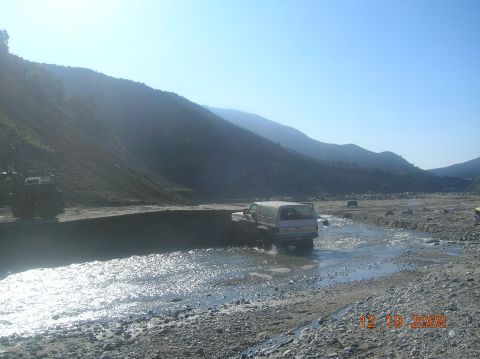 1985 Ford Bronco - Multiple vehicles navigate a shallow river in a mountainous, arid landscape.