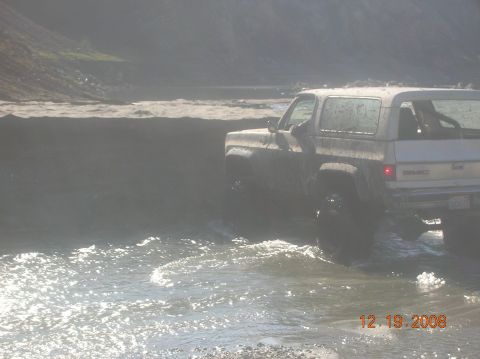 1985 Ford Bronco - A white GMC SUV navigates through shallow water, kicking up spray.