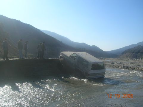 1985 Ford Bronco - A white SUV is stuck in a river with several people watching.