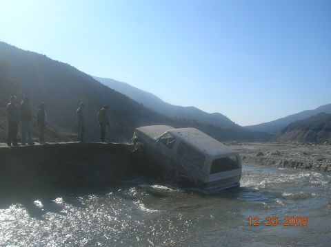 1985 Ford Bronco - A white SUV is stuck in a river, with several people watching from the bank. The date 12-20-2008 is visible in the lower right corner.