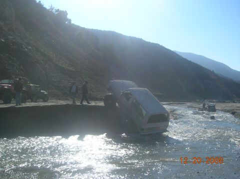 1985 Ford Bronco - Off-road vehicles navigate a challenging riverbed terrain under a clear sky.