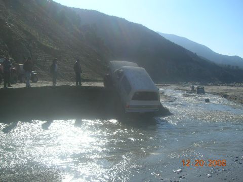 1985 Ford Bronco - Multiple vehicles navigate a riverbed on a sunny day.