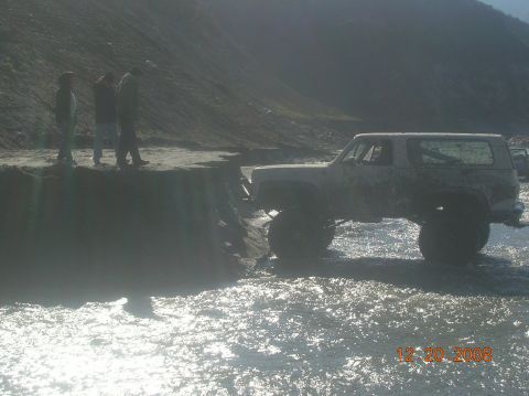 1985 Ford Bronco - Modified SUV navigates through water with onlookers present.