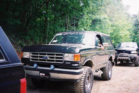 1991 Ford Bronco - A black Ford Bronco is parked on a dirt road with another truck in the background.