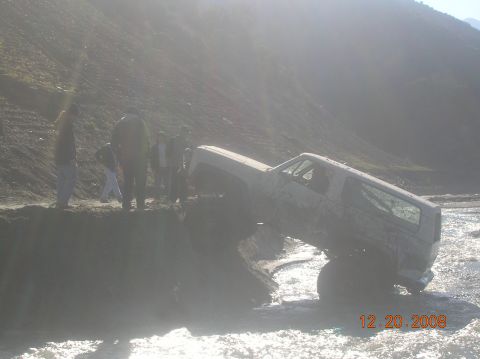 1985 Ford Bronco - A white SUV is stuck in a body of water, with several people observing the scene.