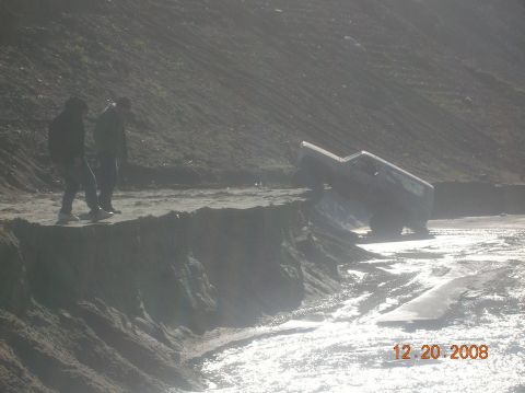 1985 Ford Bronco - A vehicle is stuck on the edge of a sandy embankment with two people observing the situation.