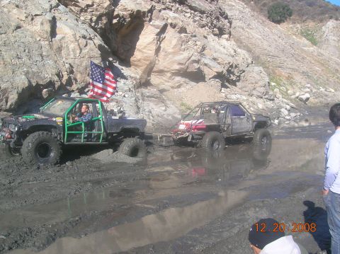 1985 Ford Bronco - Modified trucks navigate a muddy terrain with an American flag flying from one of the vehicles.