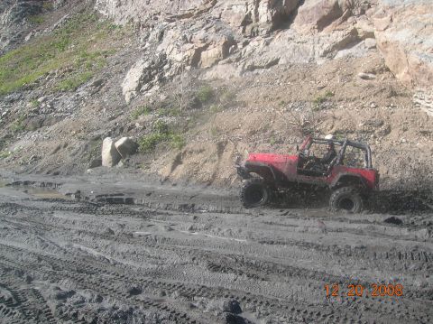 1985 Ford Bronco - A red off-road vehicle navigates a muddy terrain with tire tracks visible.