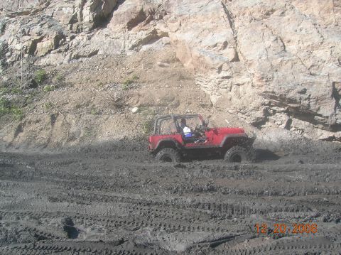 1985 Ford Bronco - A red jeep navigates a muddy trail with a rocky incline overhead. The date 12.20.2008 is visible in the lower right corner.