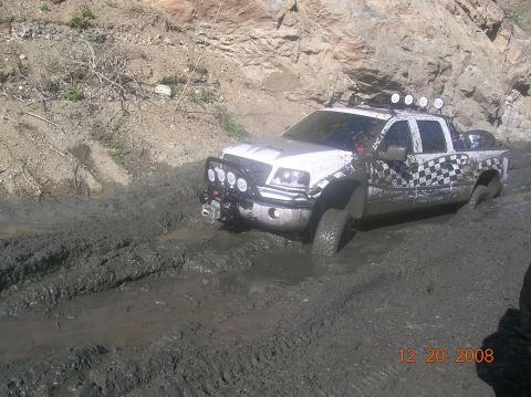 1985 Ford Bronco - Pickup truck is stuck in mud with its tires submerged.
