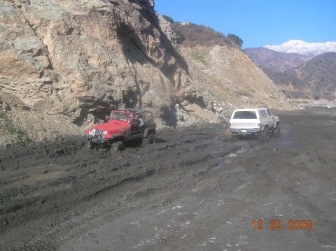1985 Ford Bronco - Two vehicles are stuck in deep mud, with one being towed by the other.