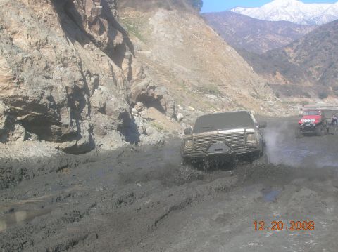 1985 Ford Bronco - Off-road vehicles tackle a challenging muddy path in a mountainous area.