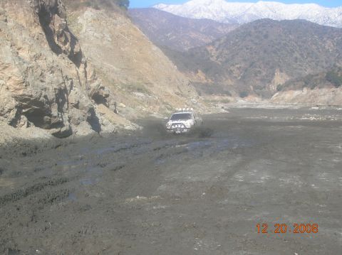 1985 Ford Bronco - SUV navigating a challenging muddy terrain with snow-capped mountains visible in the distance.