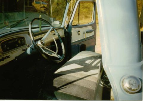 1966 Ford F-100 - The interior of a vintage pickup truck shows the driver's side dashboard, steering wheel, and seat. The door is open, revealing the exterio…