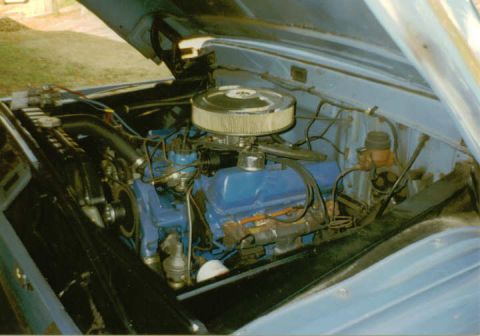 1966 Ford F-100 - The engine bay of a light blue classic Ford F-100 pickup truck is shown with the hood open. The image focuses on the V8 engine, complete wi…