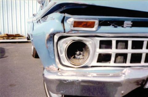 1966 Ford F-100 - Close-up front view of a damaged light blue 1960s Ford F-series pickup truck. The driver's side headlight is broken, and the front fender a…