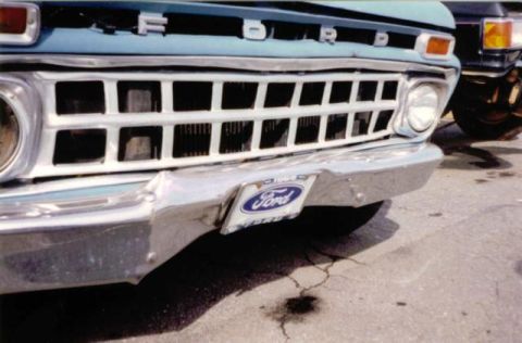 1966 Ford F-100 - The front grille and bumper of a light blue Ford pickup truck are visible. A Ford logo is present on the license plate frame.