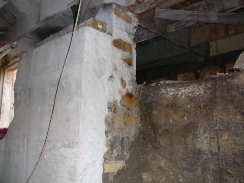 1997 Mercury Grand Marquis - A rough concrete wall with exposed brick and dirt is shown in an unfinished basement or crawl space. Wooden beams and joists are visible ov…