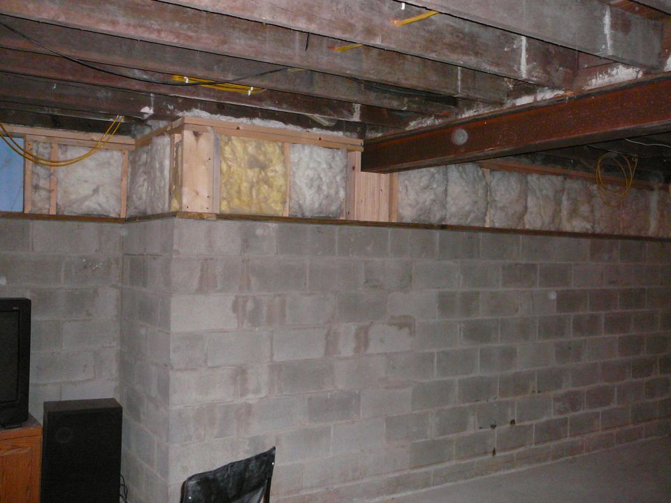 Basement with concrete block walls, exposed wooden beams, and insulation