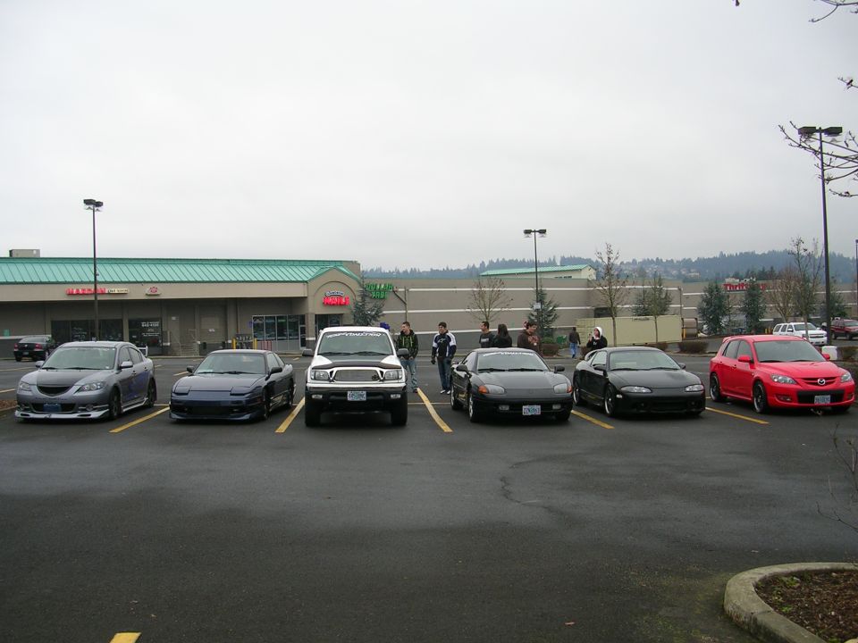 Several cars parked in a lot in front of a retail building.