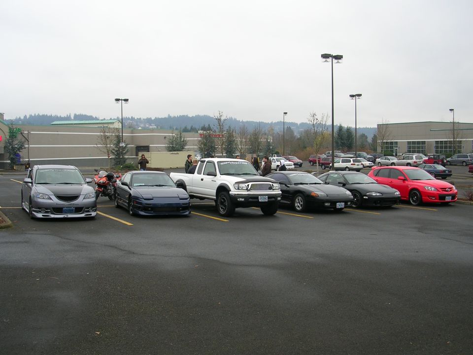 Silver Mazda 3, blue Nissan 240SX, white Toyota Tacoma, black Mitsubishi 3000GT, black Mitsubishi Eclipse, red Mazda 3 in a parking lot.