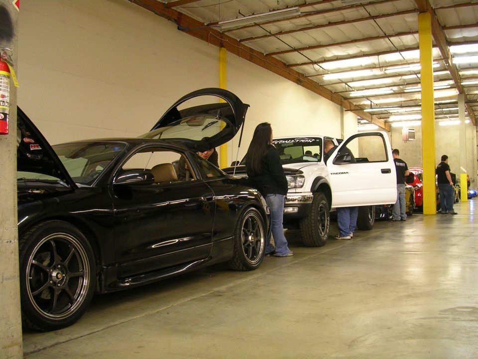 Black sports coupe and white pickup truck with open hoods and doors in a garage.