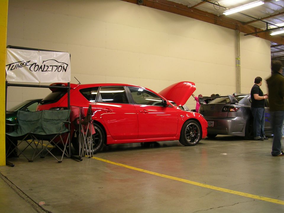Red hatchback with hood open and tuner coalition banner.