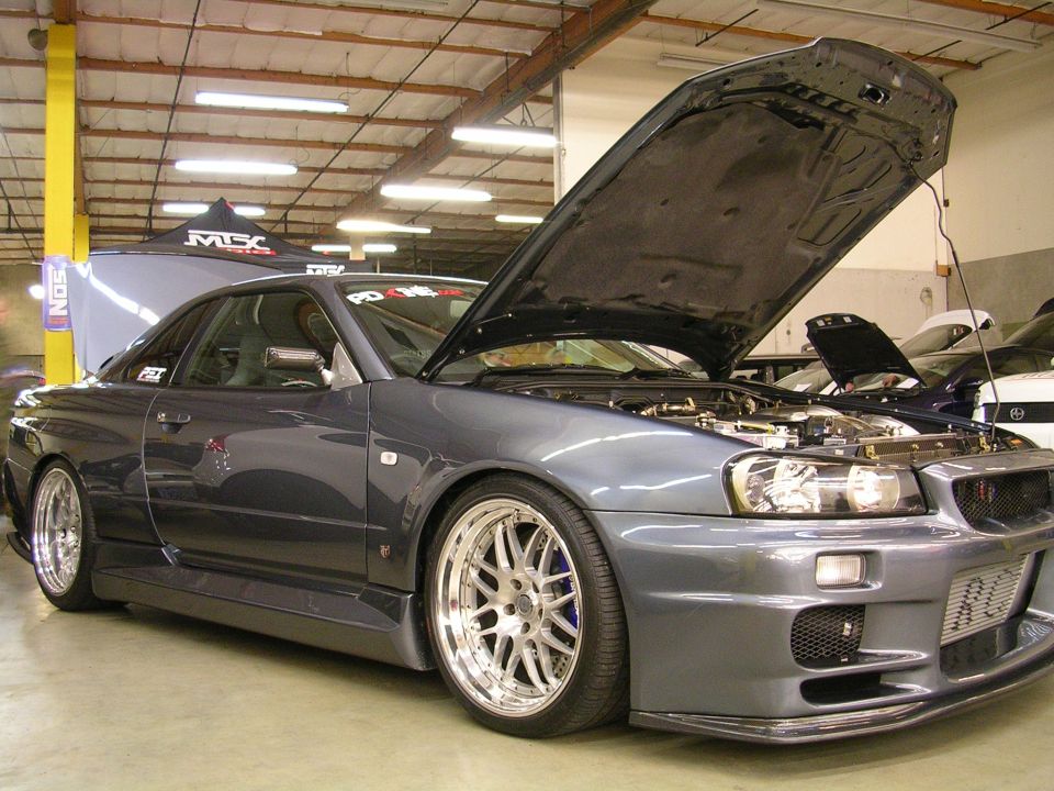 Dark gray coupe with hood open, custom wheels, parked indoors.