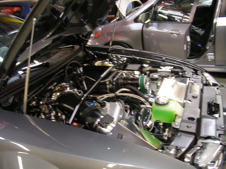 Engine bay of a gray car with aftermarket modifications, including a green coolant reservoir.