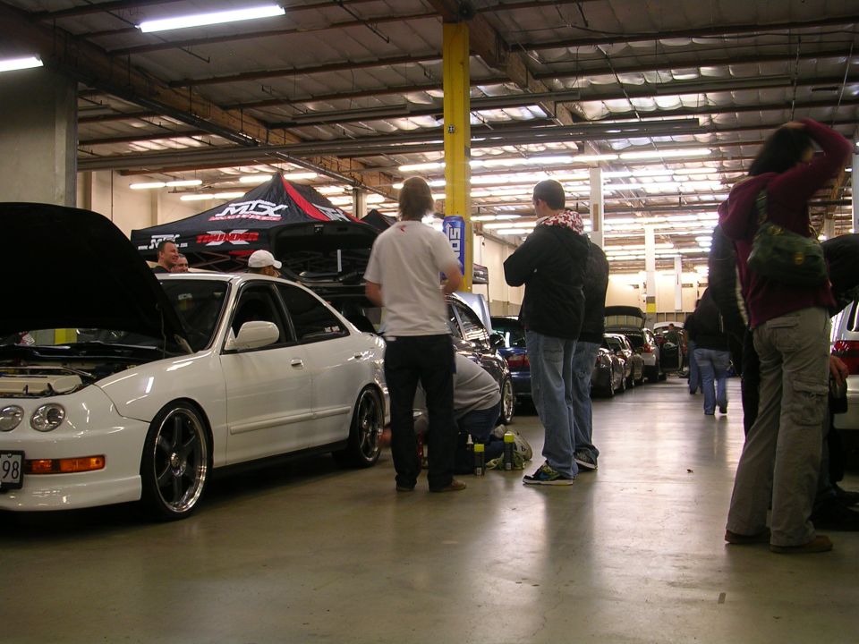 White Acura Integra coupe with hood up, parked indoors at an event.