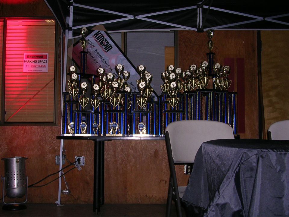 Trophies displayed under a tent with a reserved parking sign and red illuminated window.