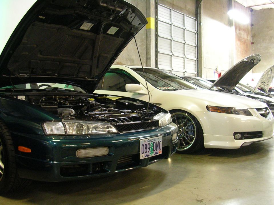 Dark green Nissan Silvia S14 and white Acura TL with hoods open in a garage.
